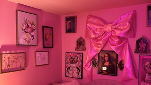 Ein zartrosa eingerichtetes Schlafzimmer mit einem großen Bett, einer Kronleuchter und verschiedenen gerahmten Bildern an den Wänden.