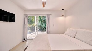 A bedroom with a bed, a television mounted on the wall, and a window with curtains. - Villa Cookies | Tropical Hideaway & Plunge Pool (Puerto Viejo de Talamanca)