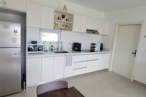 Eine moderne Küche mit weißen Schränken, einem Edelstahl-Kühlschrank, einer Mikrowelle, einer Kaffeemaschine und einem Spülbecken.