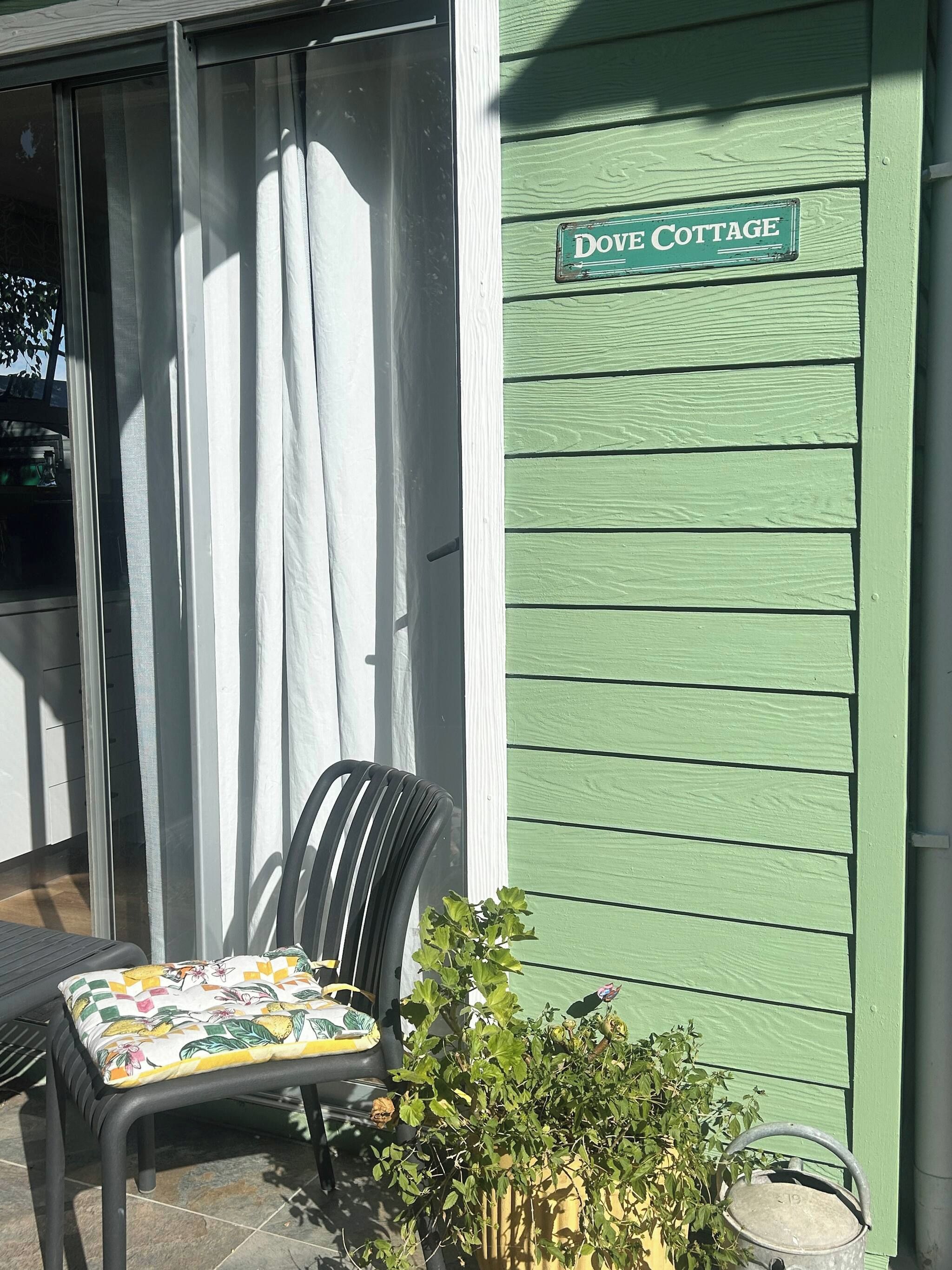 Ein Stuhl mit Blumenkissen vor einem Gebäude, das ein Schild mit der Aufschrift 'DOVE COTTAGE' zeigt.