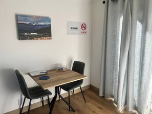 A room with a wooden table, two black chairs, a framed picture on the wall, a 'NO SMOKING' sign, and a window with grey curtains. - Charming Dove Cottage, Tranquil Retreat in Cape Town (Cape Town)