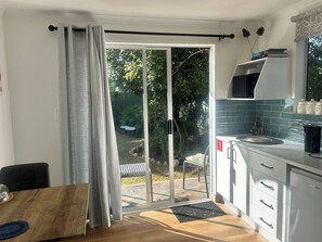 A modern kitchen with a microwave, sink, and cabinets, a dining area with a table and chairs, and a sliding glass door leading to a garden.