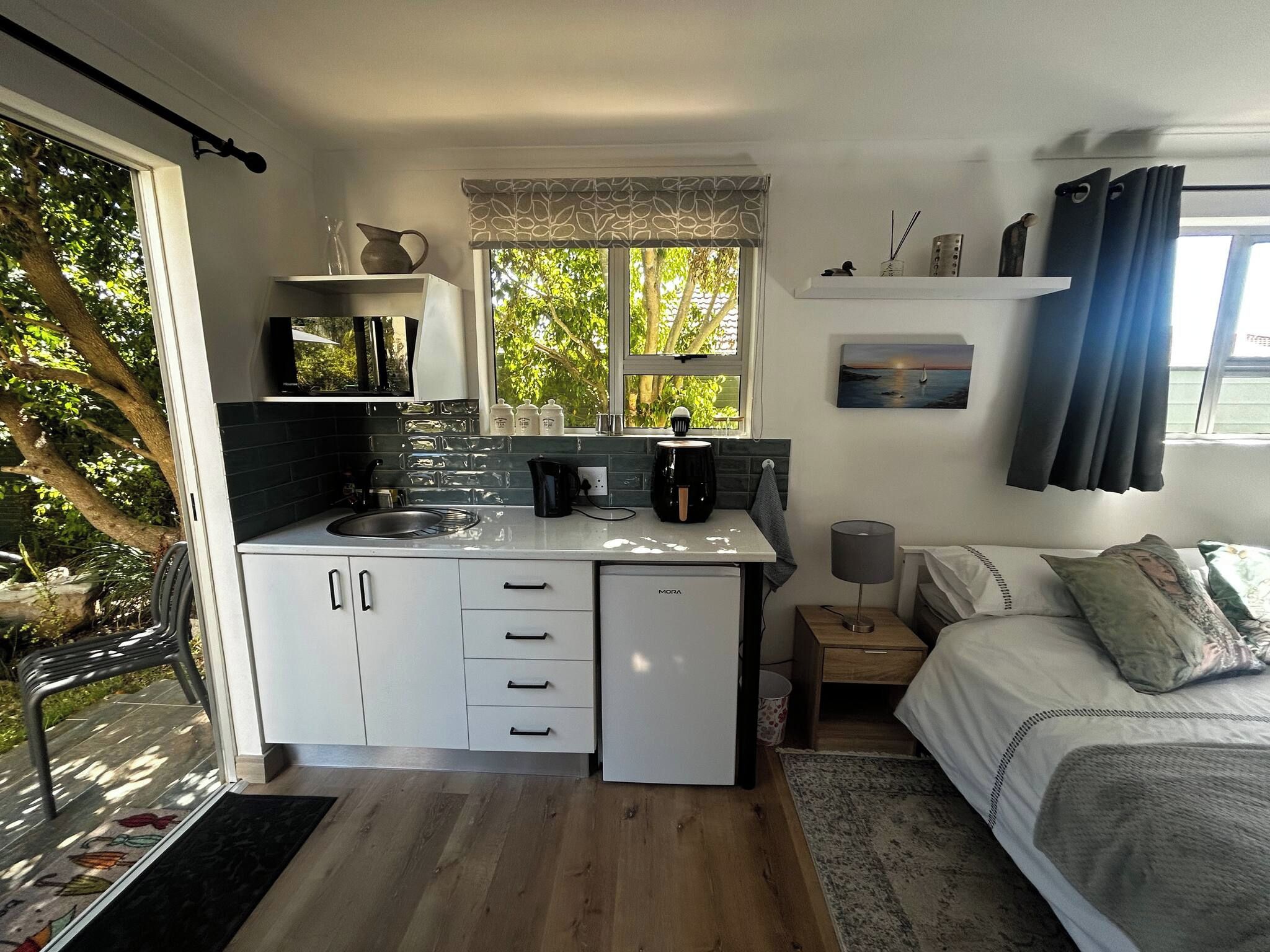 Una cocina compacta con refrigerador, lavamanos y ventana con vista a árboles.