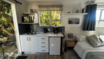 Una cocina compacta con refrigerador, lavamanos y ventana con vista a árboles.