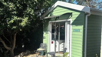 Uma pequena casa de campo verde com alpendre, duas cadeiras e um vaso de planta.