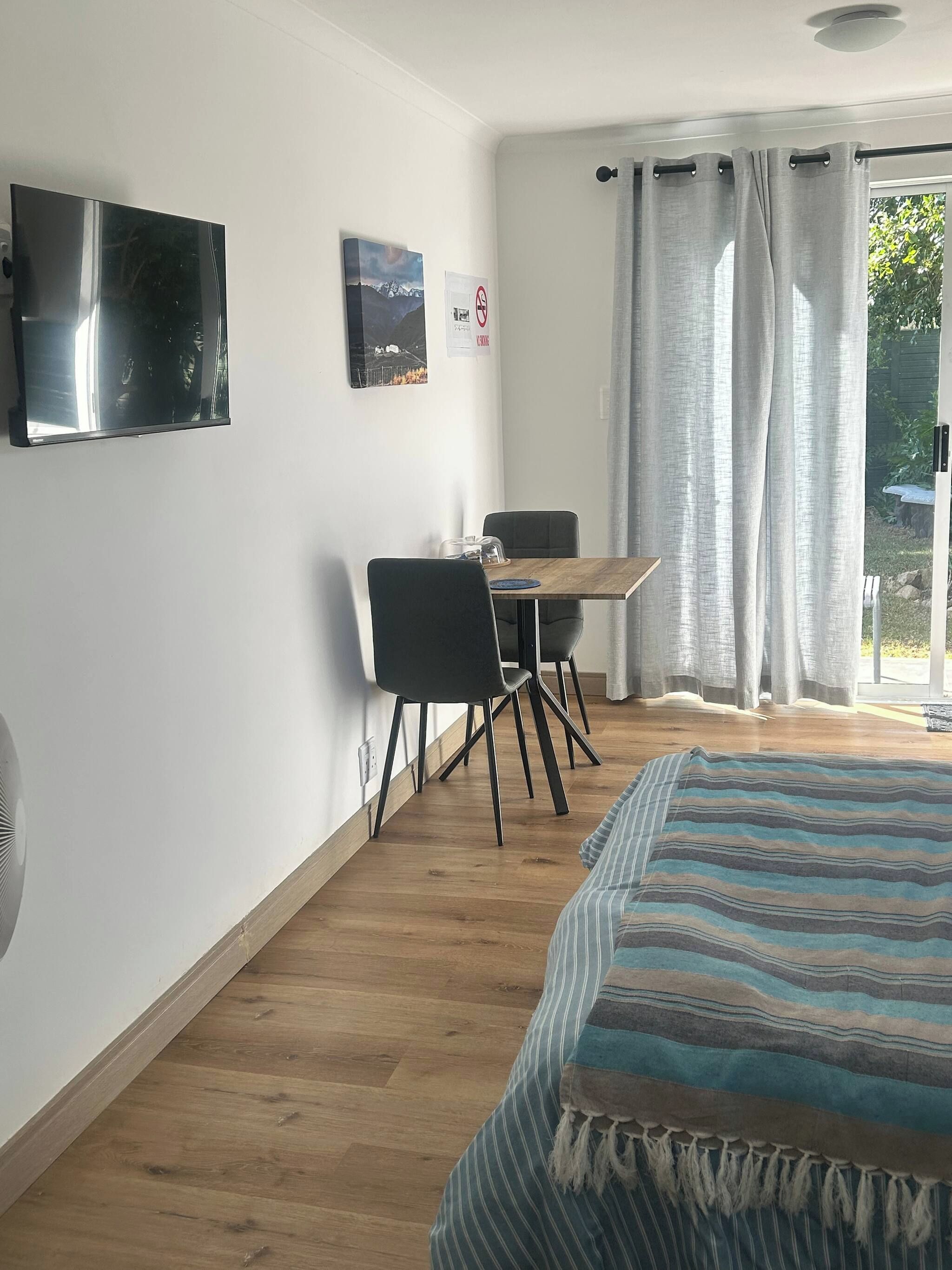 Una habitación con cama, una mesa con sillas, televisión y ventana con cortinas.