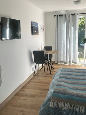 A room with a bed, a table with chairs, a television, and a window with curtains.