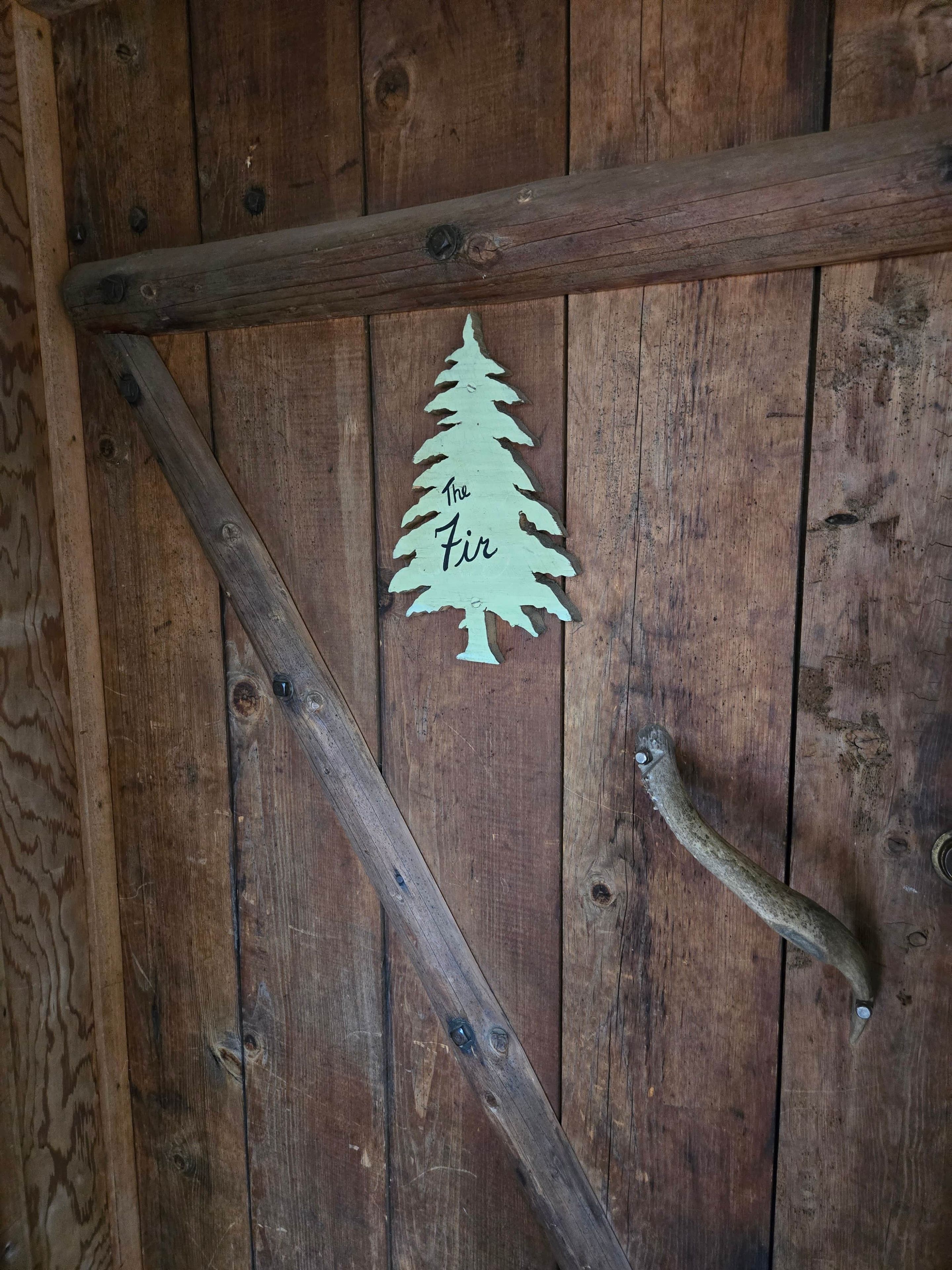 En dörr av trä med ett metallhandtag och en utskuren julgran, och texten ”The Fir” (”Granen”).