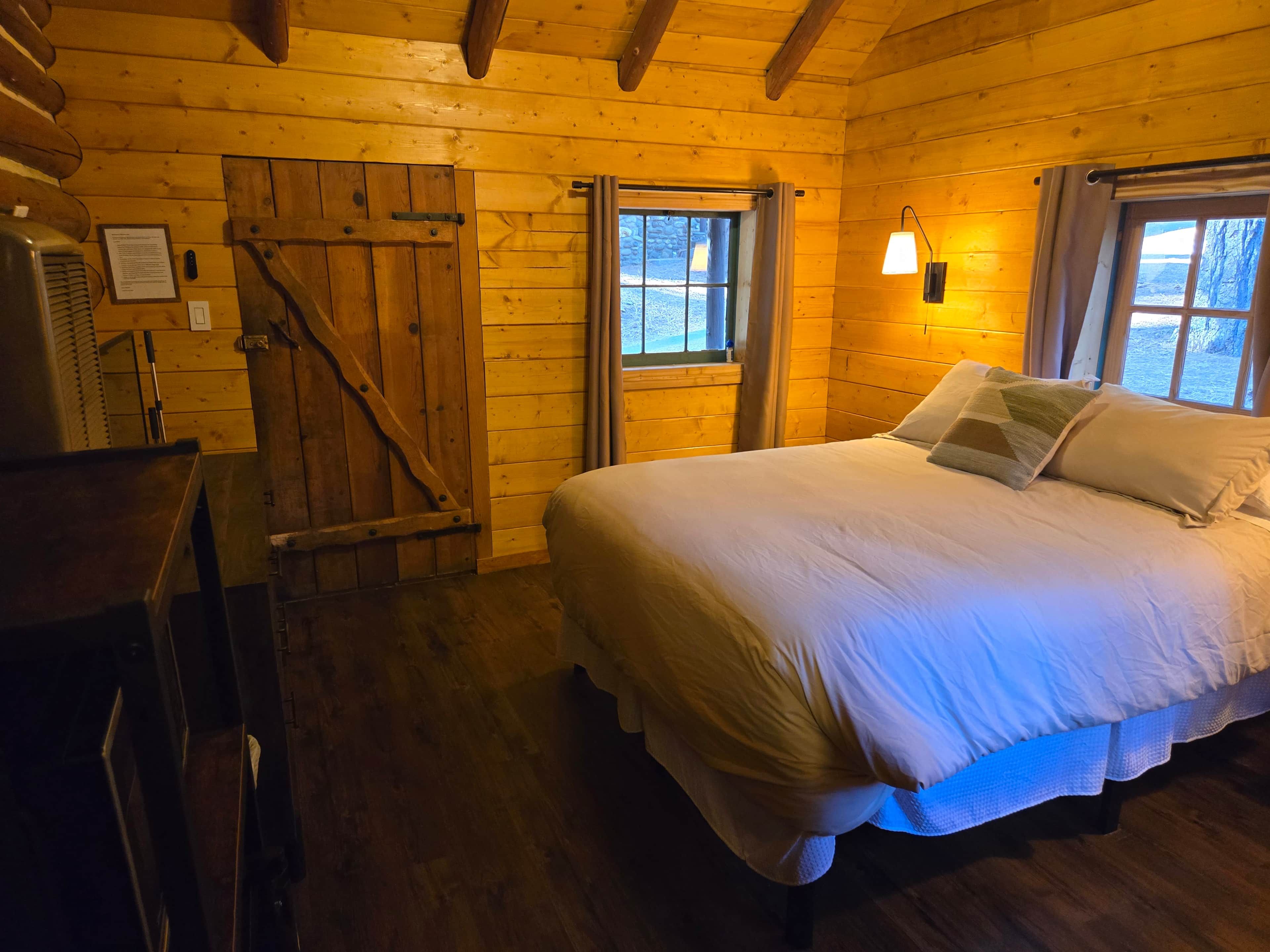 A wooden cabin bedroom with a bed, a desk, and a window.
