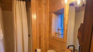 Ein Badezimmer einer Holzhütte mit Badewanne, Toilette, Waschbecken und einem beleuchteten Spiegel.