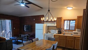 A cozy cabin interior with a wooden dining table, chairs, a kitchen with a stove, refrigerator, and a TV mounted on the wall. - Sequoia - Rustic Log Cabin (Sierra City)