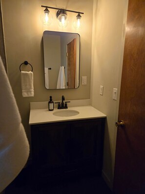 A bathroom with a white sink, a mirror above it, and a towel hanging on a ring.