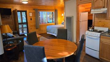 Interior de una cabaña con una cama, mesa de comedor, sillas, una cocina con estufa y un televisor.