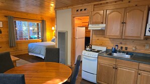 A cabin with a bed, a dining table, a kitchen with a stove, and wooden cabinets.