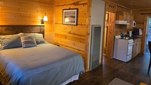 Ein Holzhütten-Interieur mit einem Bett, einer Küchenzeile und einem gerahmten Bild an der Wand.