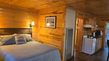 A wooden cabin interior with a bed, a kitchenette, and a framed picture on the wall.