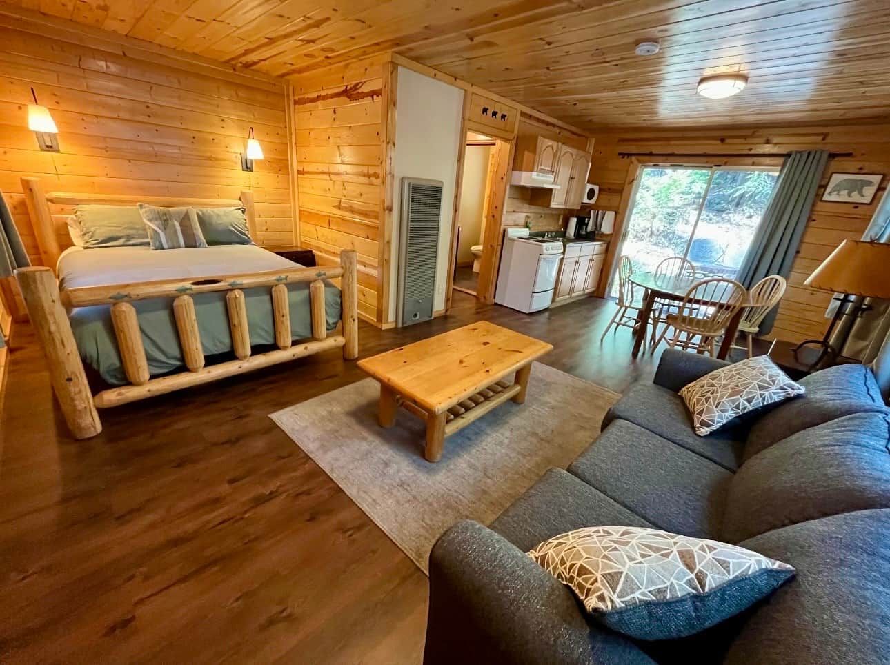 En stuga byggd av timmer med en säng, soffa, matbord och ett litet kök.