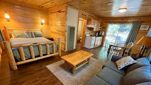 A log cabin interior with a bed, sofa, dining table, and kitchenette.