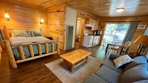 Een inrichting van een blokhut met een bed, bank, eettafel en kitchenette.