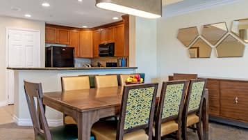 A modern kitchen with wooden cabinets, a black refrigerator, and a dining area with a wooden table and patterned chairs.