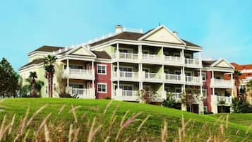 A multi-story hotel with balconies and a grassy hill in the foreground.