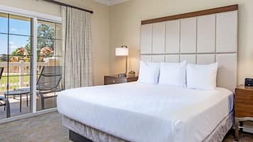 A hotel room with a large bed, two bedside lamps, a wooden nightstand, and a view of a patio with outdoor furniture.