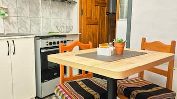 Une cuisine compacte équipée d’une cuisinière, d’un four et de meubles de rangement en bois. On y trouve une table à manger avec des chaises, et une plante en pot posée sur la table.