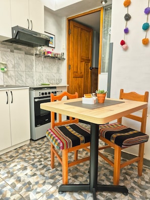 A compact kitchen with a stove, oven, and wooden cabinets. There is a dining table with chairs, and a potted plant on the table.