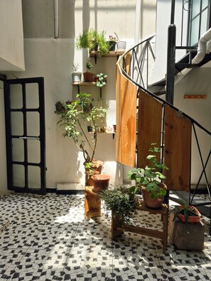 A sunlit interior with a tiled floor, a wooden staircase, and various potted plants.
