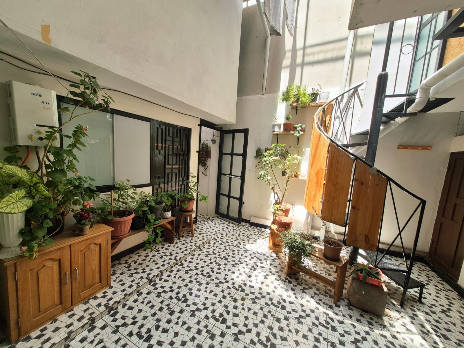 A room with a tiled floor, a wooden cabinet, and multiple potted plants.