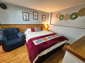 A bedroom with a bed, a chair, a bedside table, a lamp, and wall decorations.