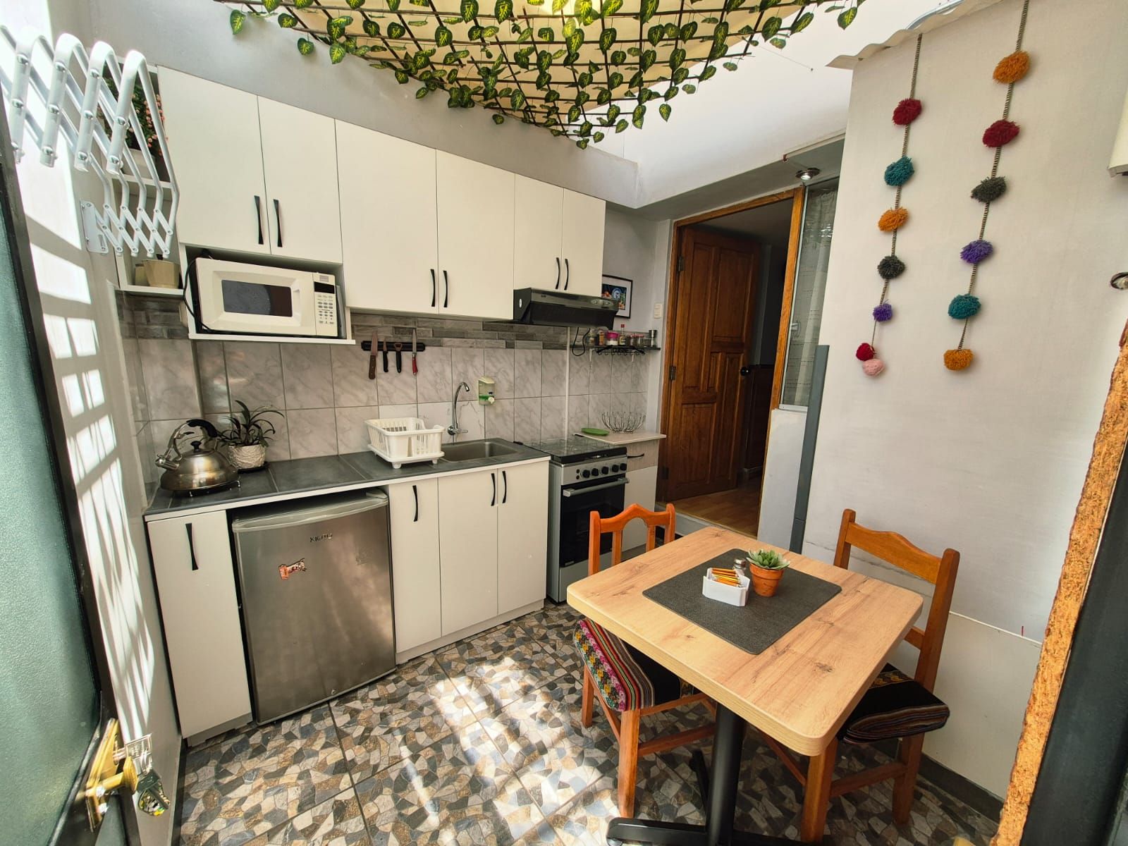 A compact kitchen with a microwave, stove, and sink. There is a dining table with chairs and a small potted plant.