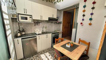 A compact kitchen with a microwave, stove, and sink. There is a dining table with chairs and a small potted plant.