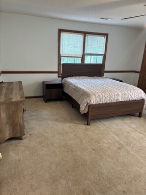 A bedroom with a bed, a nightstand, a dresser, and a window with blinds.