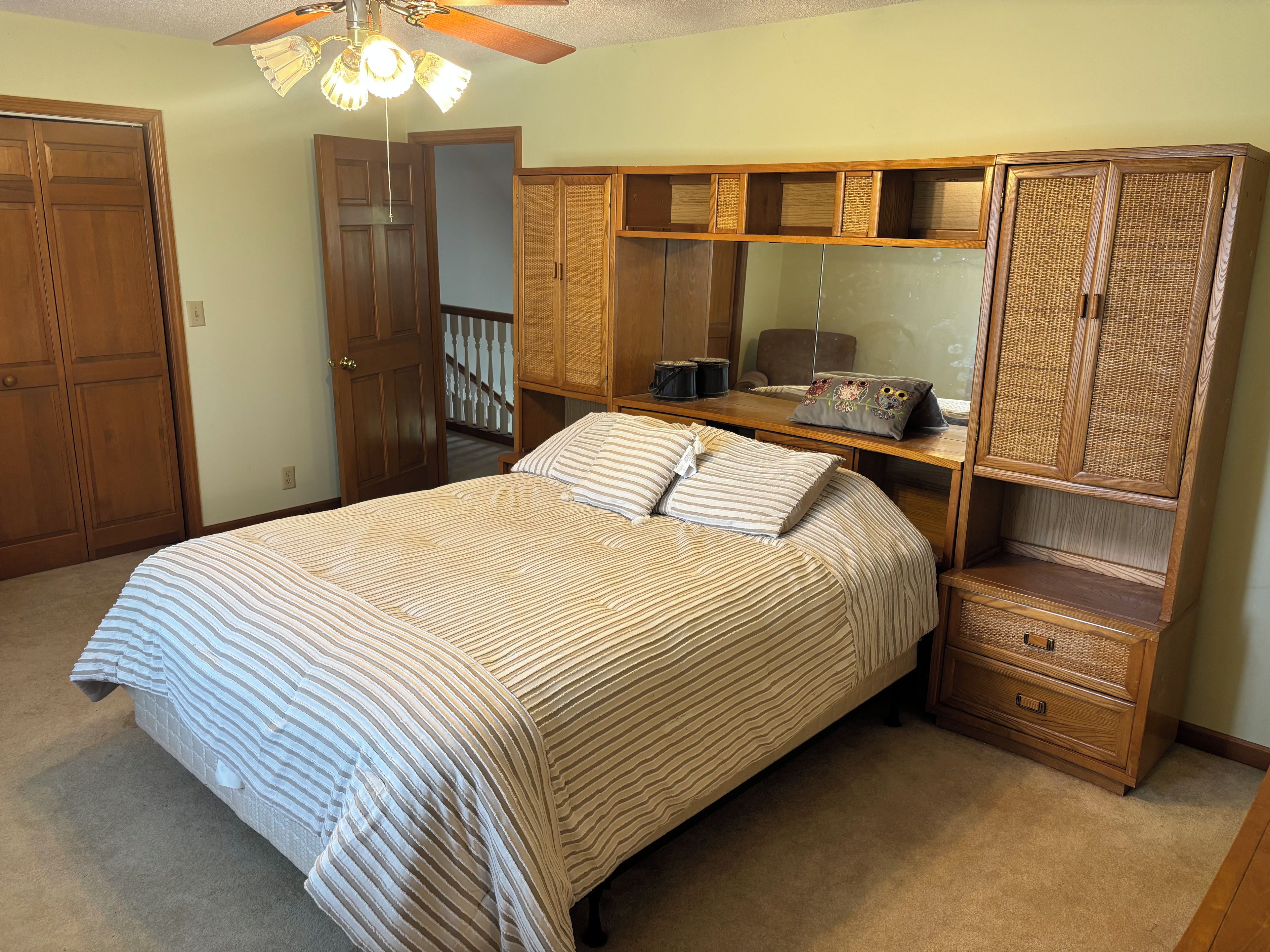 Une chambre à coucher avec un lit, une armoire en bois et un ventilateur de plafond.