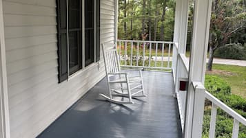 Une véranda couverte avec une chaise berçante, une balustrade blanche et une fenêtre avec des volets.
