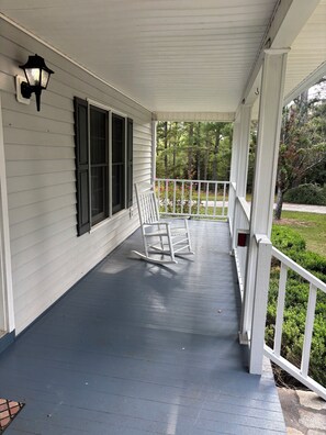 A covered porch with a rocking chair, a white railing, and a window with shutters.