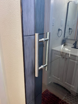 Casa de banho com cabine de chuveiro em vidro, puxador de porta em aço inoxidável e lavatório com torneira preta.