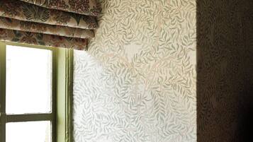 A room corner with patterned wallpaper and a window with a green trim.