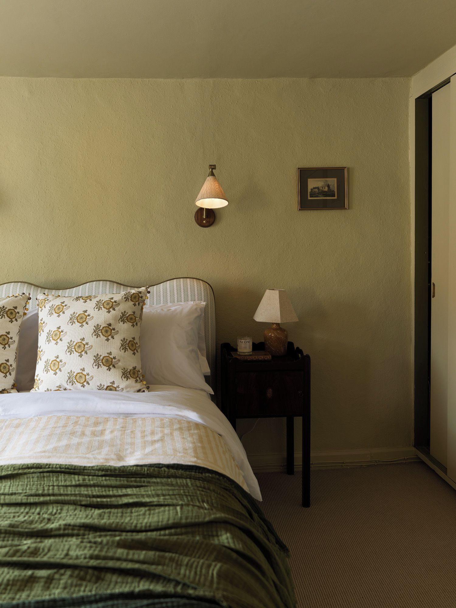 Un dormitorio con cama, mesita de noche, lámpara de pared y un cuadro enmarcado.