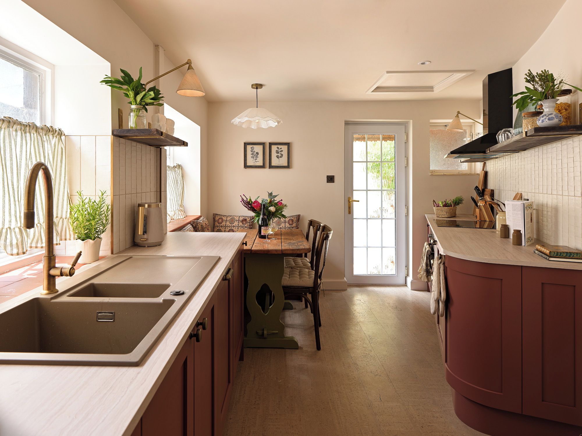 A modern kitchen with a central island, a dining area with a table and chairs, and a view of the outdoors through a door.