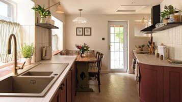 A modern kitchen with a central island, a dining area with a table and chairs, and a view of the outdoors through a door.