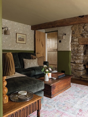 A cozy living room with a dark sofa, a wooden coffee table, and a stone wall. - Charming Two BD Cottage in Malmesbury (Malmesbury)
