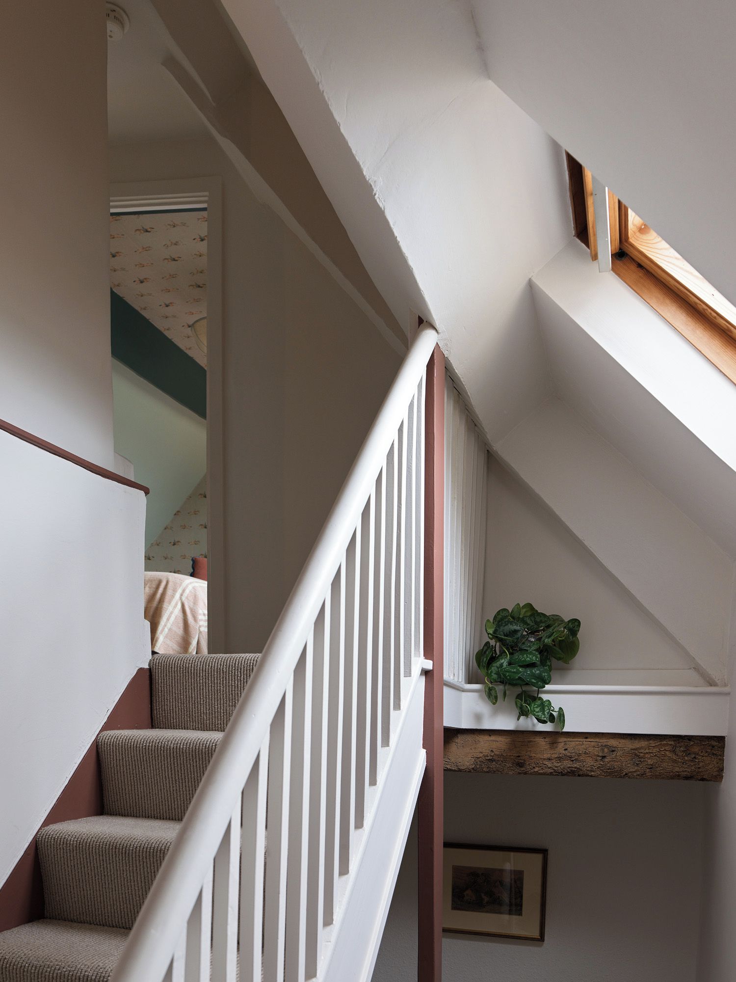 A staircase with white railings leading to a landing with a wooden beam and a potted plant.