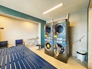 A laundry room with two wall-mounted washing machines, a bench, and a trash bin. - Fully furnished apartment 180m from the beach. (Salvador)