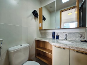 Une salle de bain comprenant des toilettes, un lavabo, un miroir et un porte-serviettes.