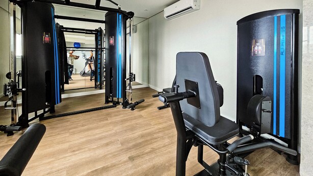 Ein Fitnessraum mit Trainingsgeräten, einem Spiegel und einer Tür zu einem weiteren Raum.