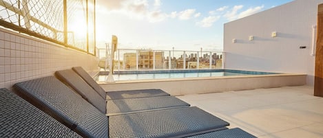 A rooftop pool area with lounge chairs and a city view.