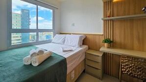 Ein Hotelzimmer mit Bett, Schreibtisch, Stuhl, Fenster mit Stadtblick und einer Zimmerpflanze.