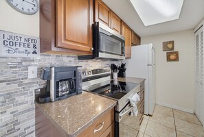 A kitchen with wooden cabinets, a microwave, a coffee maker, and a refrigerator. - Whimsical Wonders Sweetwater Club Near Disney (Kissimmee)